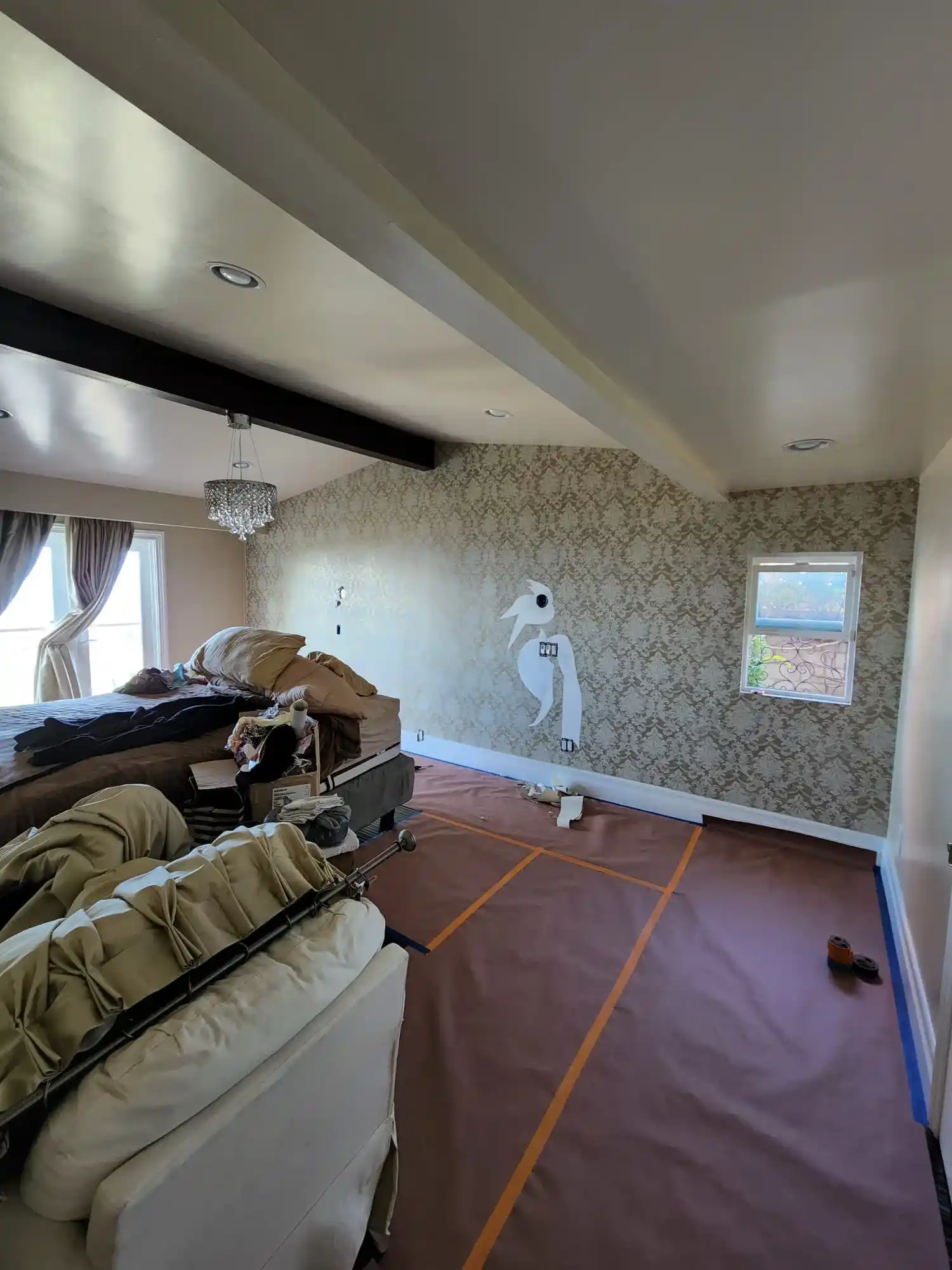 Bedroom renovation in progress with wallpapered accent wall, tray ceiling and floor protection