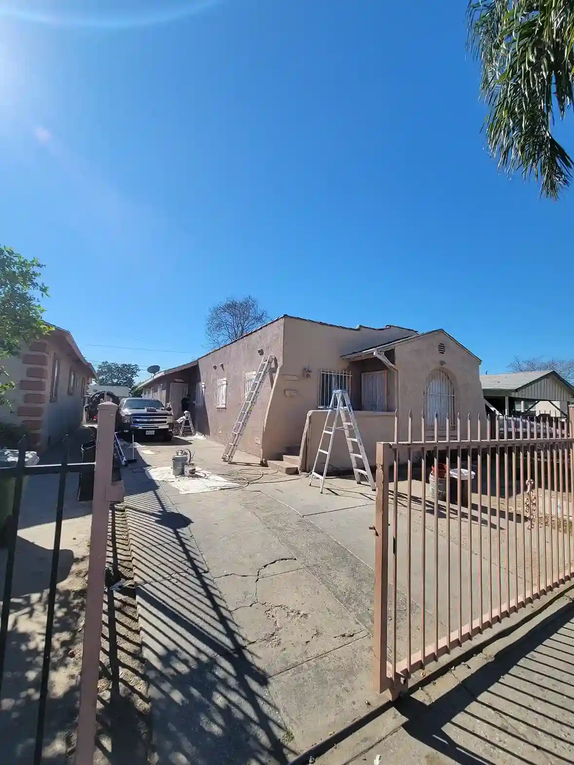 Exterior stucco home renovation with ladders and painting prep in Brooklyn NY