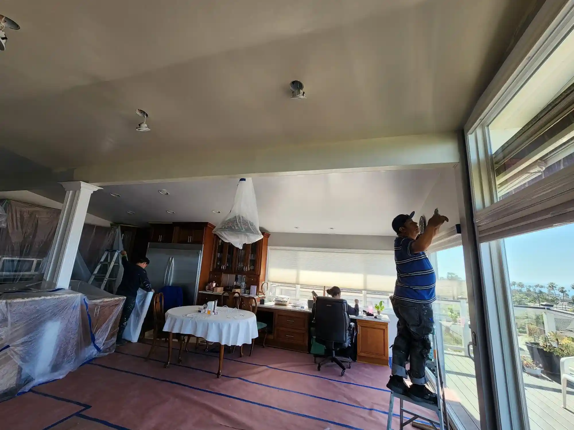 Interior home renovation in Brooklyn with workers painting ceiling and floor protection