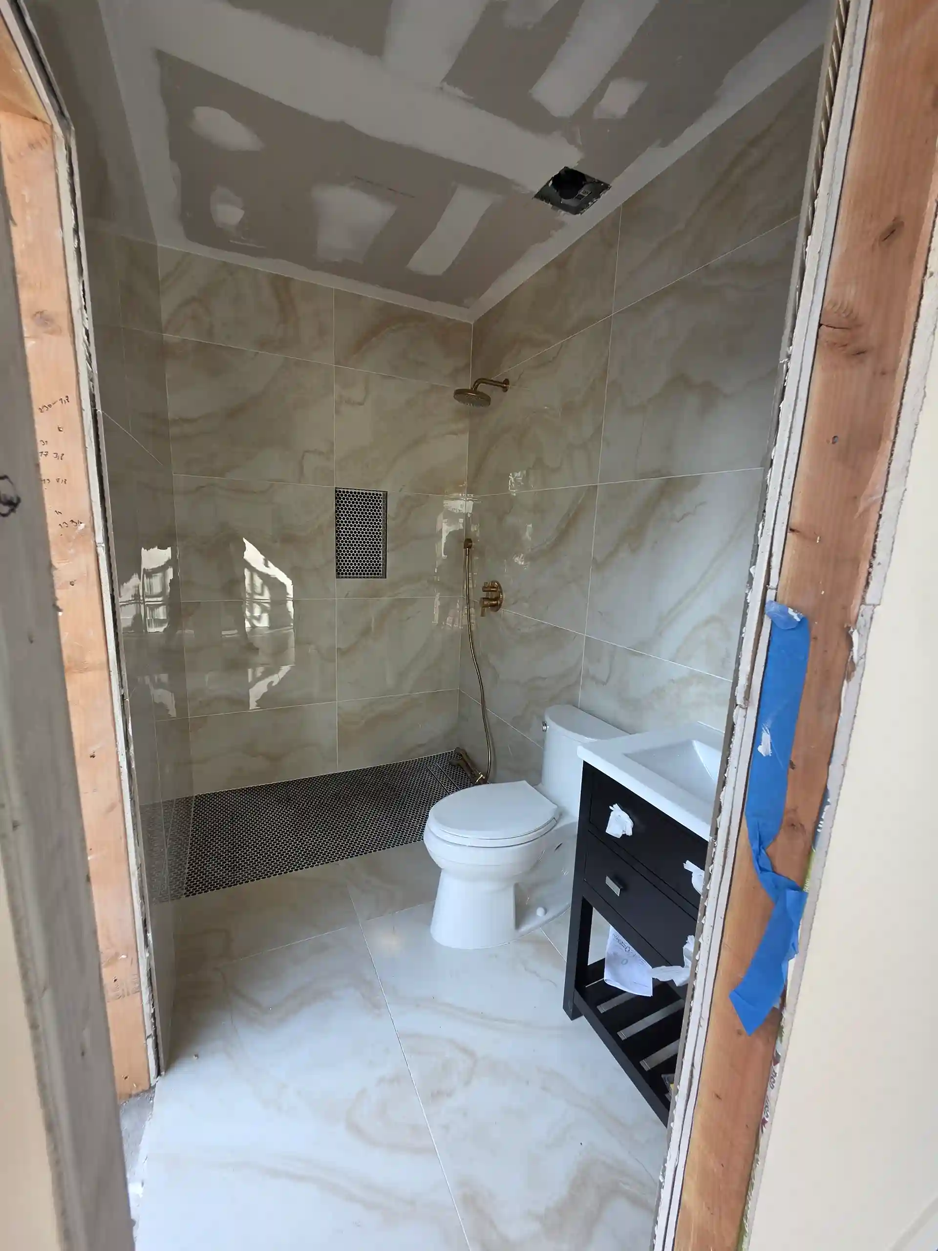 Modern bathroom renovation in progress with marble tile, brass shower fixtures and new vanity in Brooklyn NY