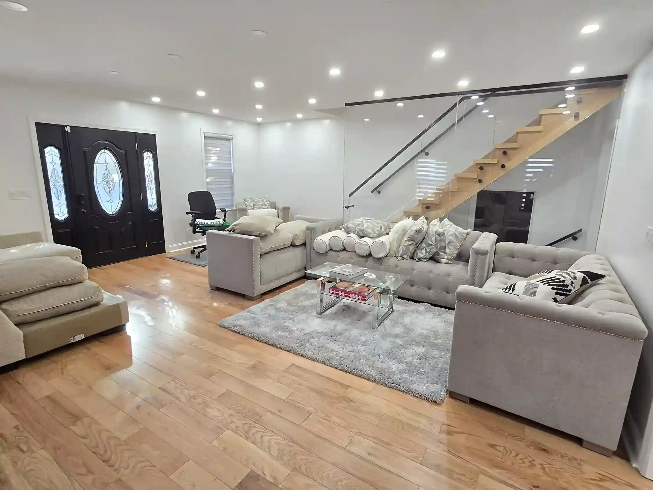 Modern renovated living room with hardwood floors, gray sofas and glass staircase in Brooklyn NY