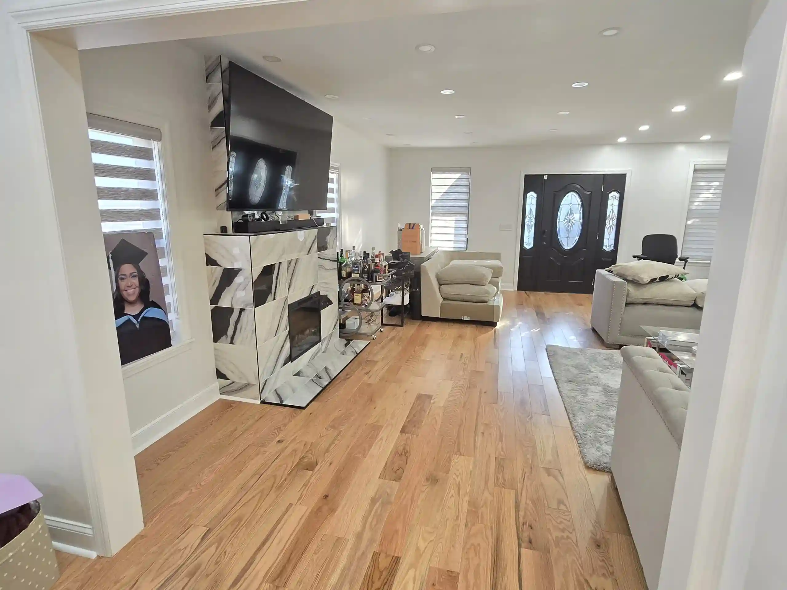 Modern renovated living room with marble TV wall, wood floors and recessed lighting in Brooklyn home