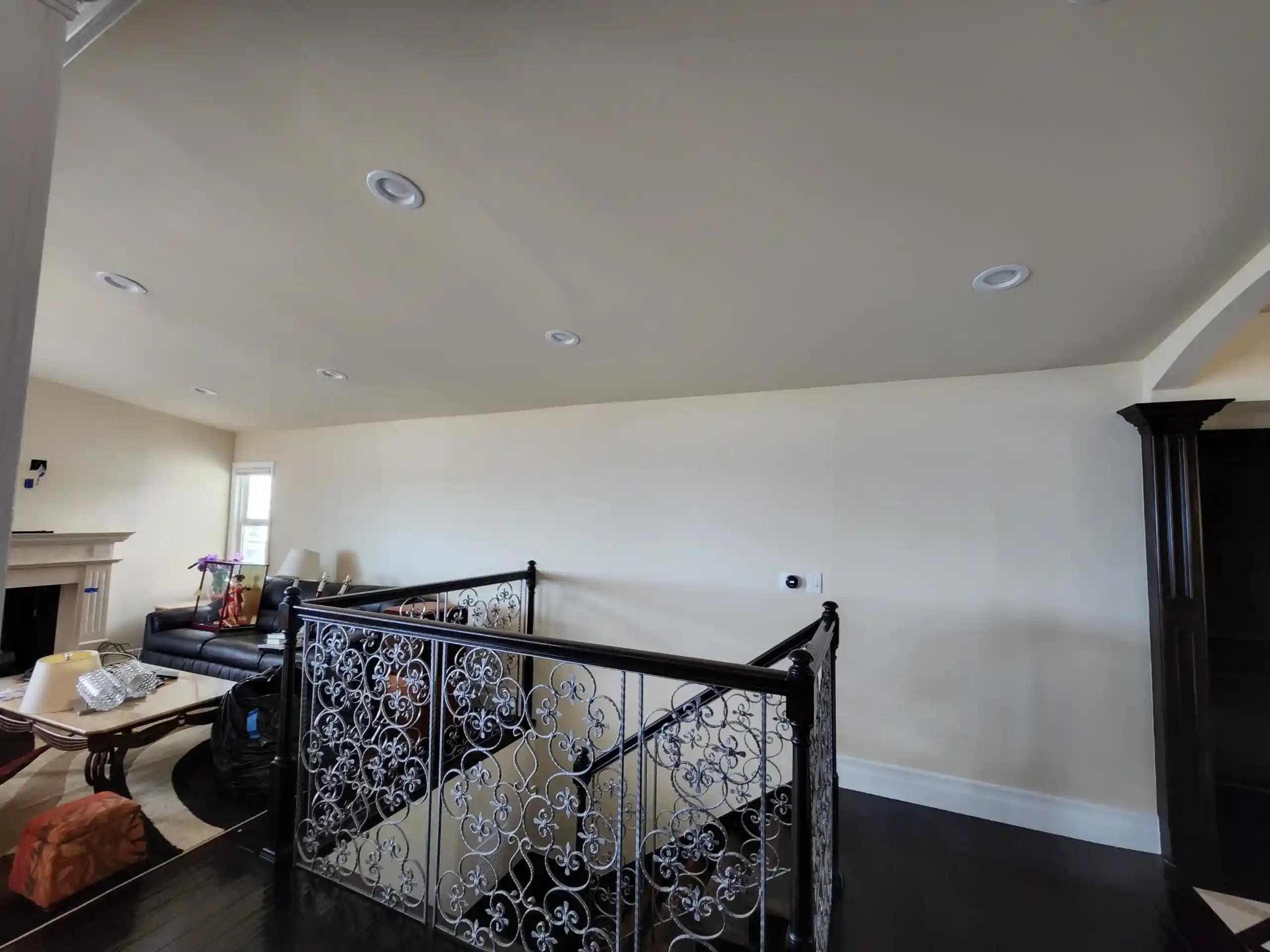 Modern living room renovation with recessed lighting, dark floors and decorative wrought iron stair railing in Brooklyn home