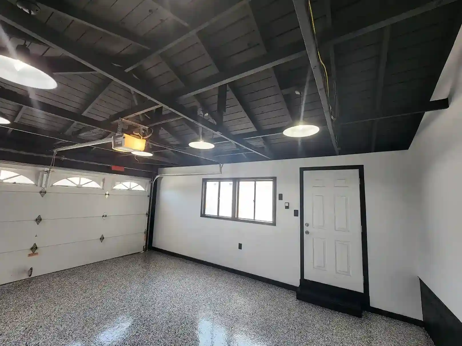 Renovated garage interior with epoxy floor, white walls and black ceiling beams in Brooklyn NY