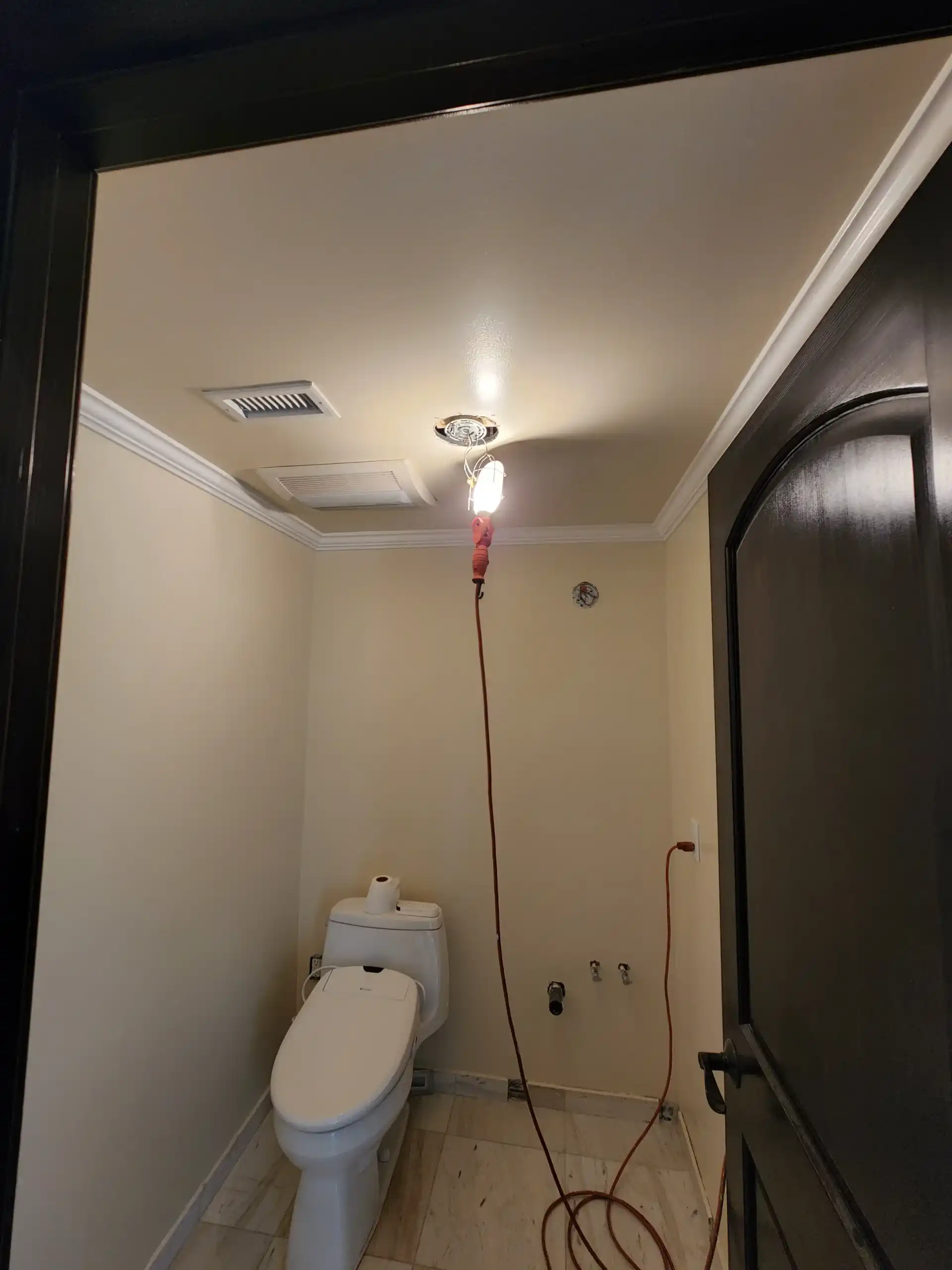 Small bathroom renovation in progress with toilet, tile floor and work light
