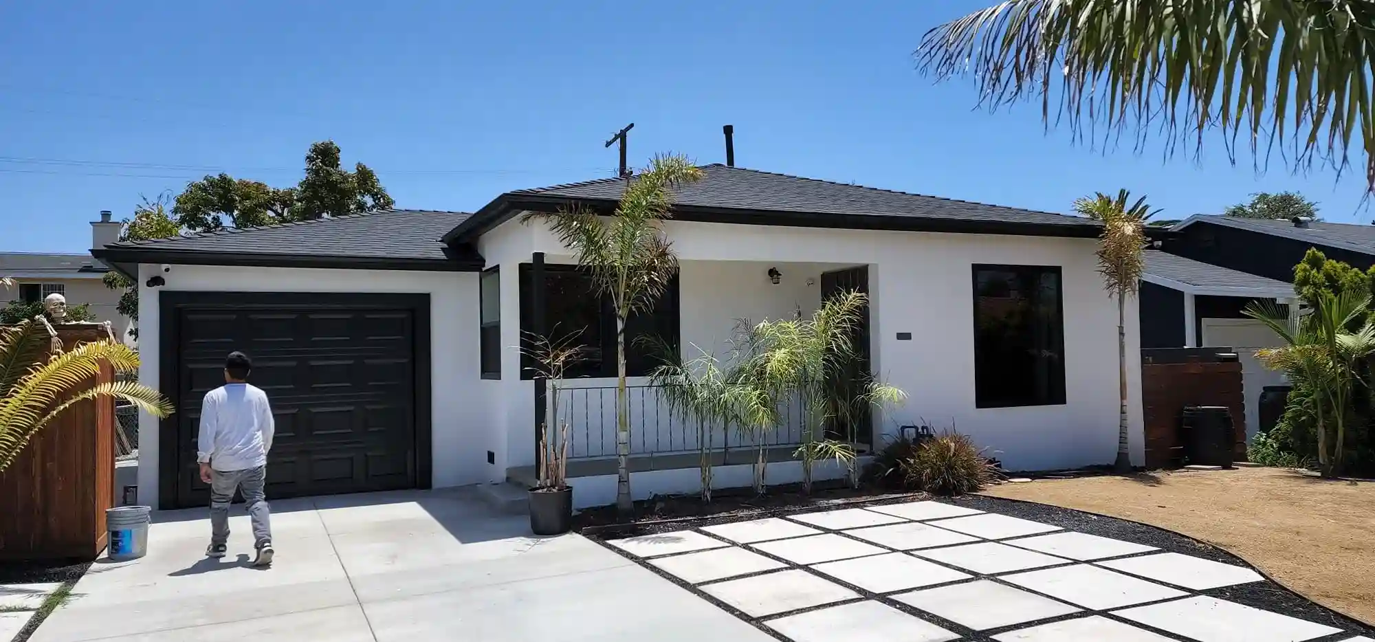 White stucco home exterior renovation with black garage door and modern concrete driveway